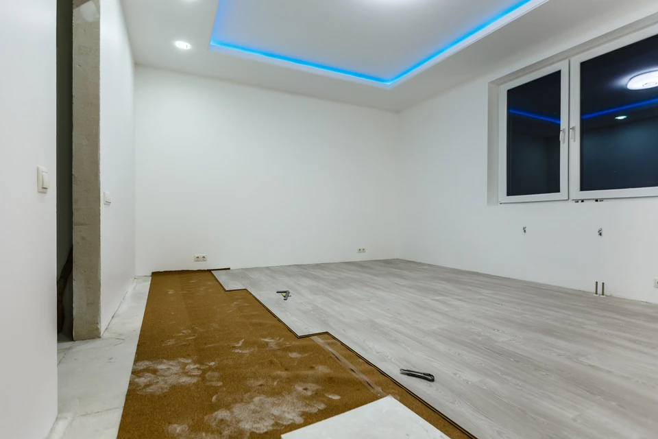 Intérieur en cours de rénovation avec pose de revêtement de sol stratifié gris clair partiellement installé sur chape béton brute