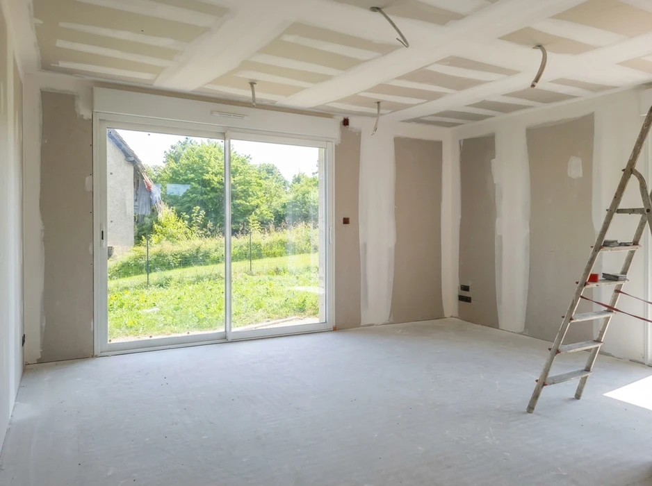 Plasterer utilisant une torche de finition pour lisser un nouveau plâtre à la surface d'un mur à l'intérieur d'une maison pendant les travaux de rénovation ou de construction