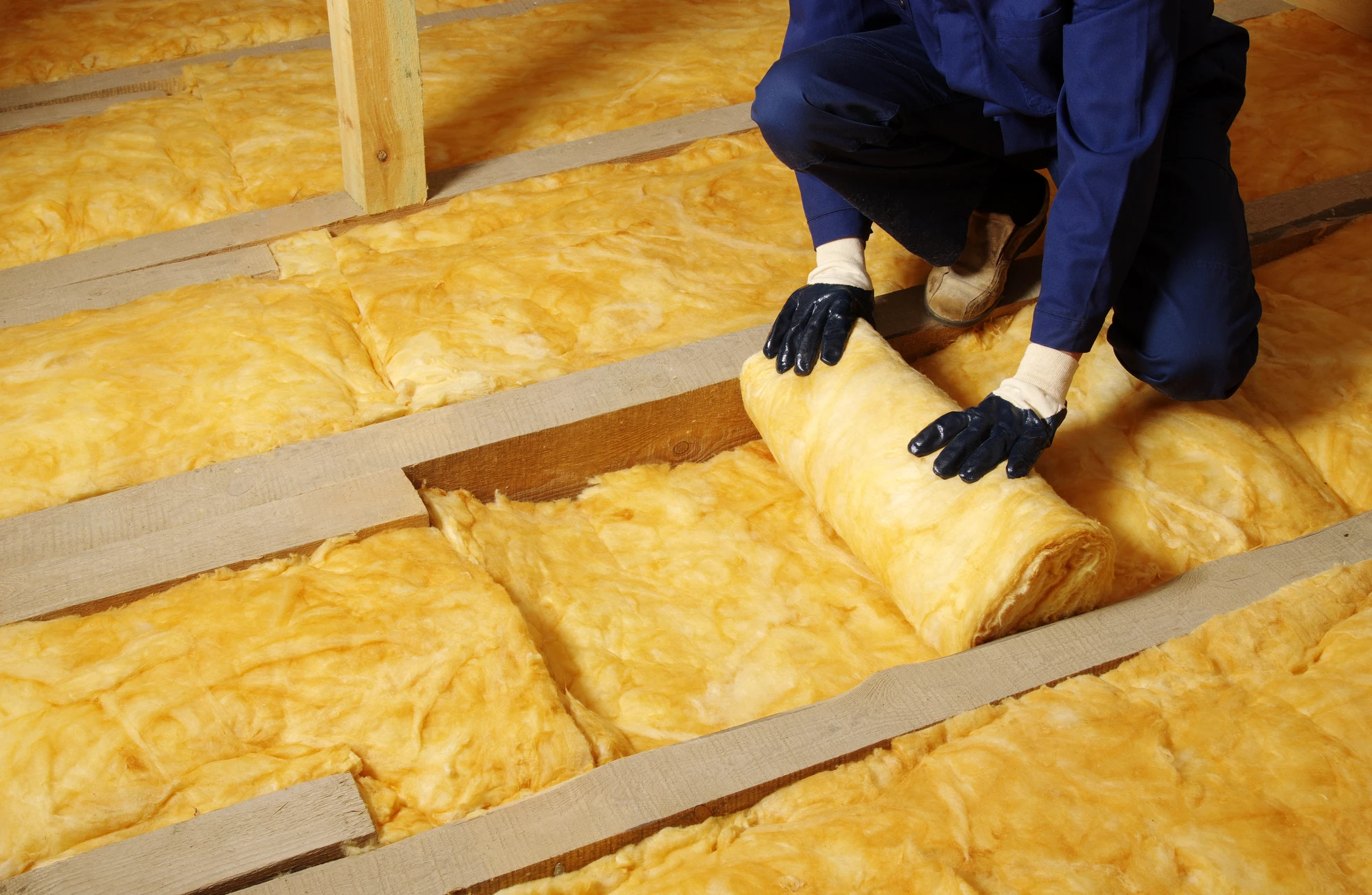 Ouvrier en combinaison de protection intégrale et masque respiratoire installant de l'isolant dans les combles d'une habitation